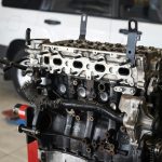Detailed view of a car engine in an auto repair shop with a blurred vehicle in the background.